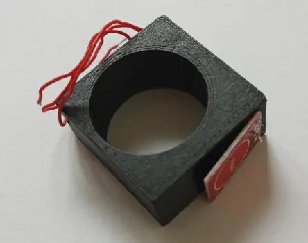 3D-printed finger ring, made from a cuboid shape with a circular hole, with an attached button and cables
